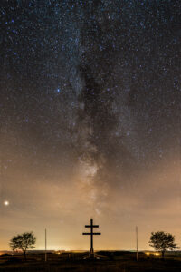 Cette photo de nuit montre la voie lactée se levant à la verticale d'une croix de Lorraine entourée de deux mats et deux arbres