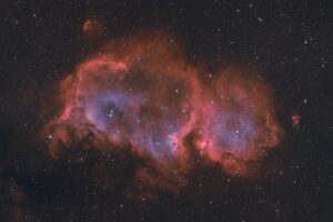Une photographie d'une nébuleuse rouge et bleutée sur fond de ciel étoilé