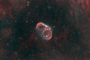 Une astrophotographie de nébuleuse rouge et verte en forme de croissant ou de méduse sur un fond de ciel étoilé