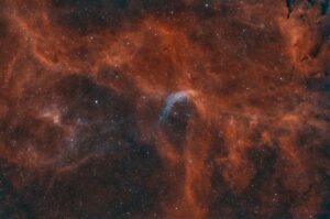Astrophotographie d'une nébuleuse dont le centre est formé d'une coquille bleue autour d'un groupe d'étoiles dans des volutes de nuages orangés