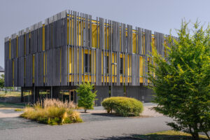 Architecture jaune recouvert de panneaux de bois et végétalisation du parking alentours